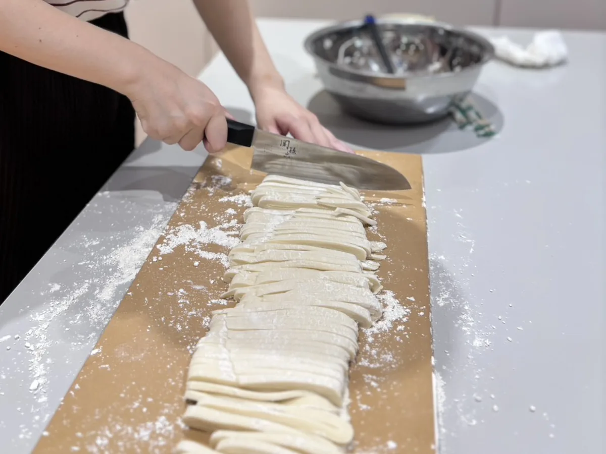 Hands carefully cutting handmade udon noodles on a floured board