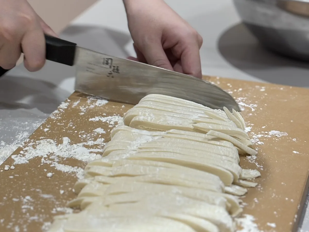 Close-up of handmade Sanuki udon noodles being cut with a knife